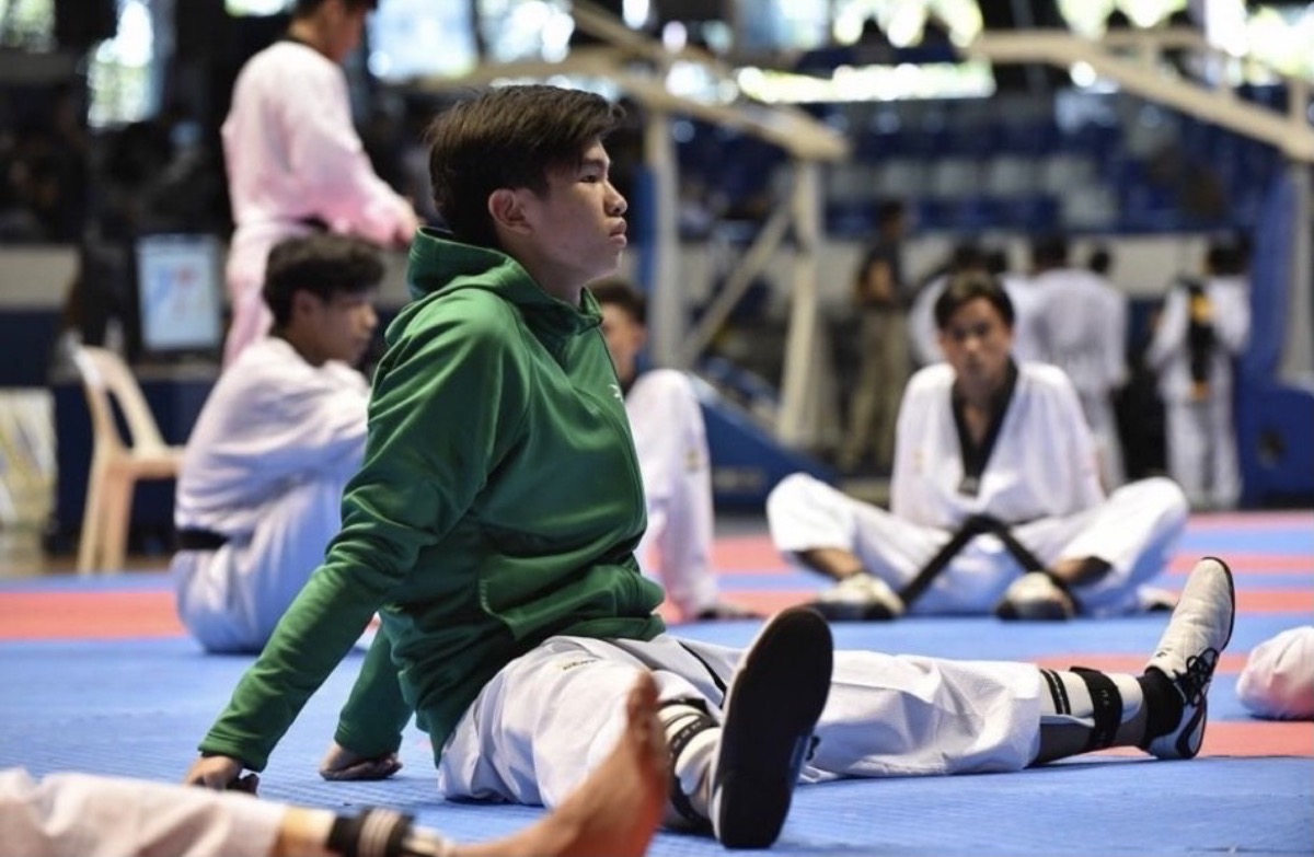 Keith Uy stretching on the mats in a green De La Salle jacket before training